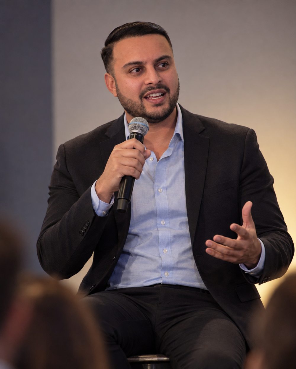 Dil Phagura speaking into a handheld microphone during a conference panel.